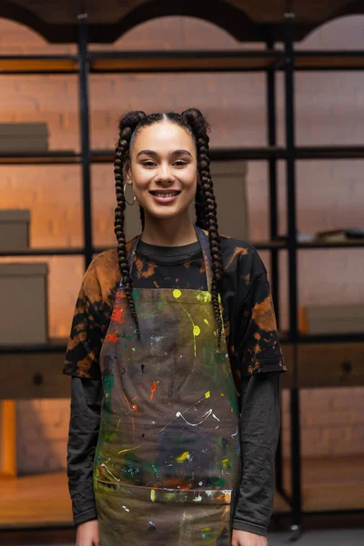 Cheerful african american craftswoman in apron looking at camera in workshop — Stock Photo