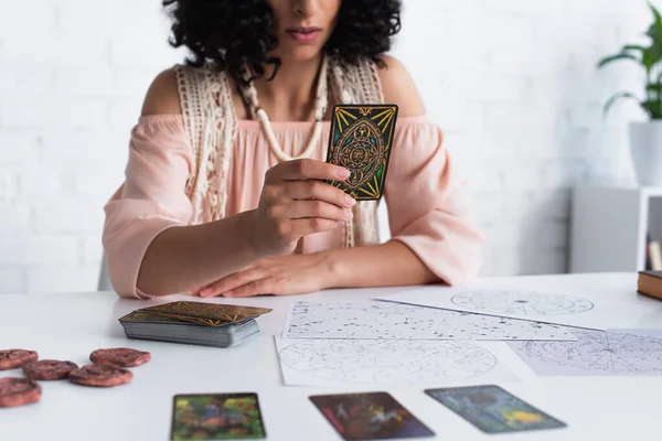 KYIV, UKRAINE - JUNE 29, 2022: cropped view of blurred astrologer holding tarot card near celestial charts — стоковое фото