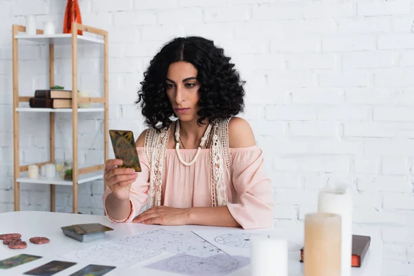 KYIV, UKRAINE - JUNE 29, 2022: brunette astrologist looking at tarot card near constellation charts — Photo de stock