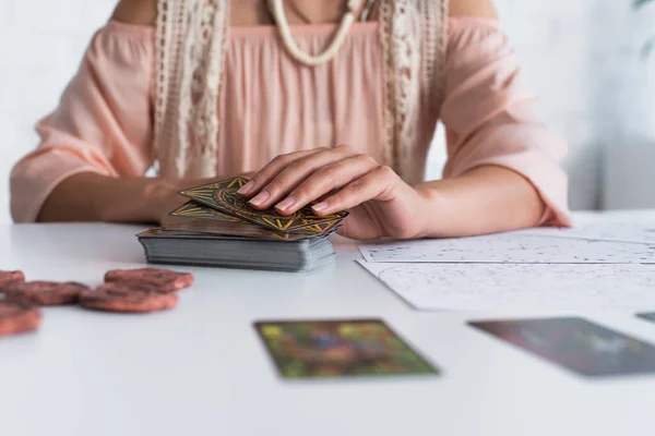 KYIV, UKRAINE - JUNE 29, 2022: partial view of blurred fortune teller holding tarot cards near star charts — Stockfoto