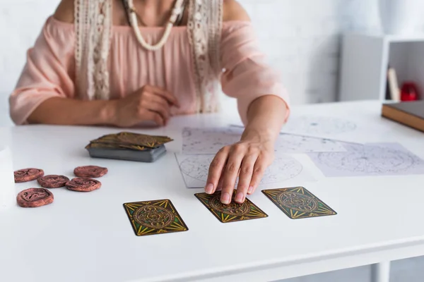 KYIV, UKRAINE - JUNE 29, 2022: cropped view of blurred astrologist taking tarot card near natal charts  and clay runes — Foto stock