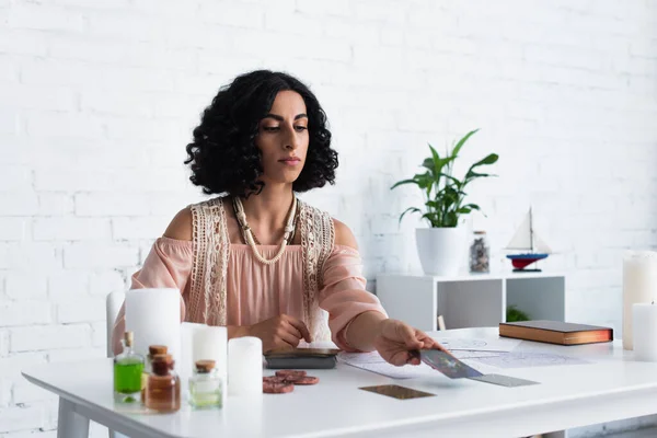 Young woman predicting on tarot cards near blurred candles and essential oils — Foto stock