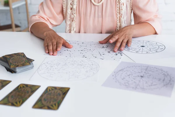 KYIV, UKRAINE - JUNE 29, 2022: partial view of young medium near astrological charts and burred tarot cards — Fotografia de Stock