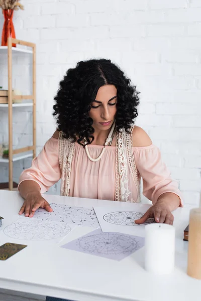 Brunette astrologist near natal charts and candles on table — стоковое фото
