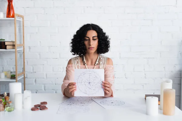 Young predictor holding star map near candles and clay runes — Foto stock