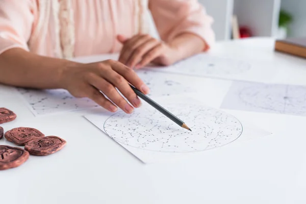 Cropped view of blurred astrologist pointing at celestials map with pencil — стоковое фото