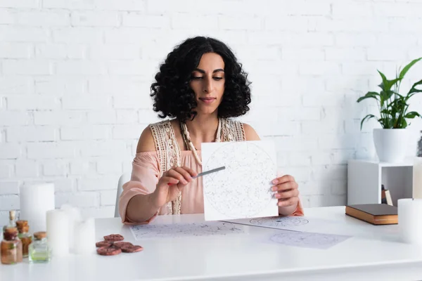 Young astrologer pointing at celestial chart near clay runes and blurred candles — Fotografia de Stock