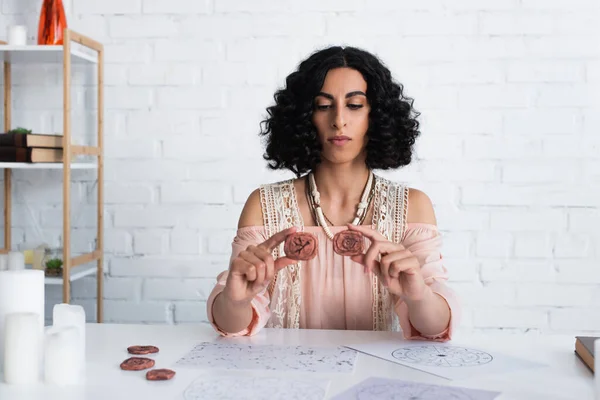 Brunette fortune teller holding clay runes near celestial charts at home — стоковое фото