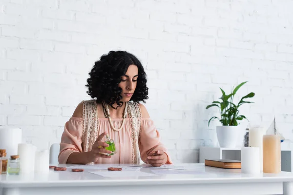 Brunette predictor holding clay rune and bottle of essential oil near candles - foto de stock