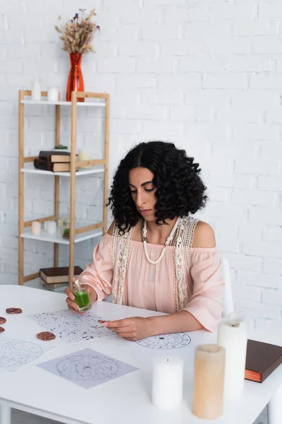 Young brunette soothsayer holding essential oil and clay rune near star charts — стоковое фото