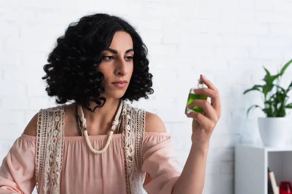 Brunette fortune teller looking at bottle with essential oil at home — Stock Photo