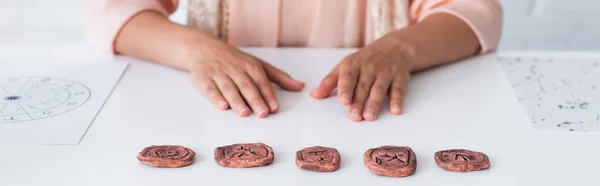 Partial view of fortune teller sitting near clay runes and star charts, banner - foto de stock