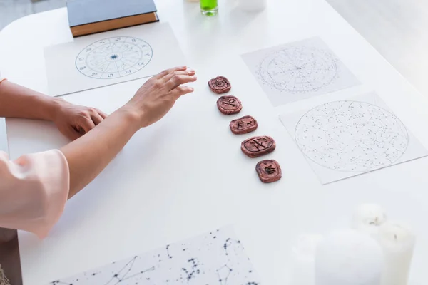 High angle view of cropped astrologist near star charts and clay runes on table — Stock Photo