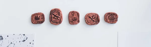 Top view of clay runes near celestial charts on white surface, banner - foto de stock