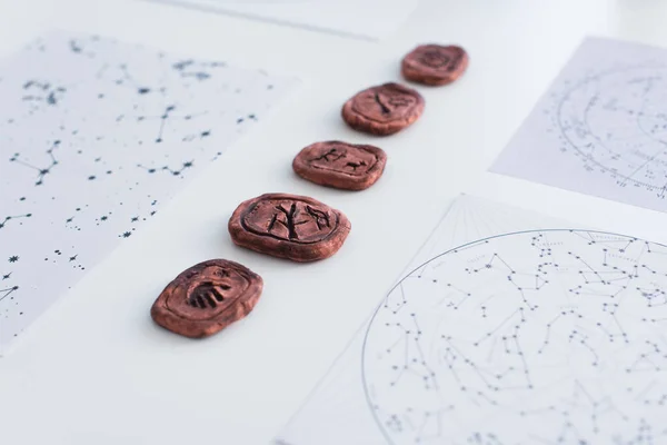 Clay runes near star charts on white surface — стоковое фото