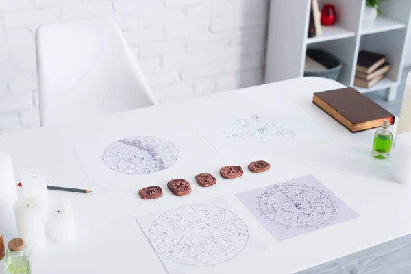 Astrological maps and clay runes near candles and prediction book on white table — Fotografia de Stock