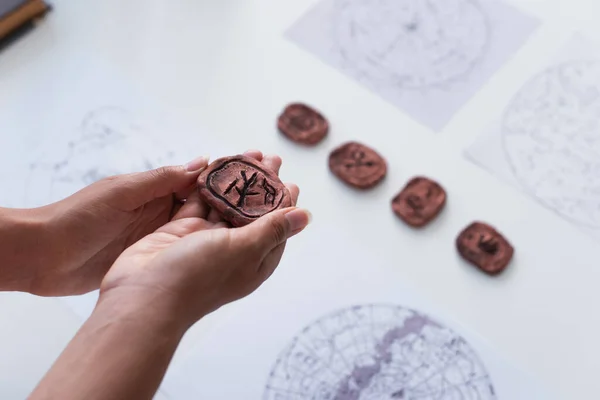 High angle view of cropped fortune teller holding clay rune near blurred star charts — Stock Photo