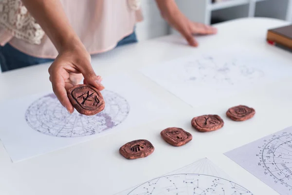 Partial view of astrologer holding clay rune near cosmic maps on table — Stock Photo
