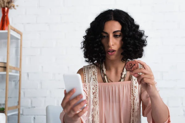 Brunette fortune teller looking at mobile phone and holding clay rune — Foto stock