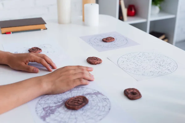 Partial view of astrologer near clay runes and constellations charts on table — Photo de stock