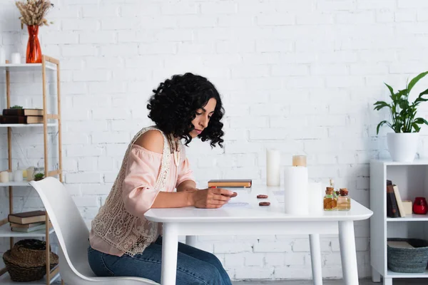 Young brunette predictor holding clay rune near candles and essential oils — Stock Photo