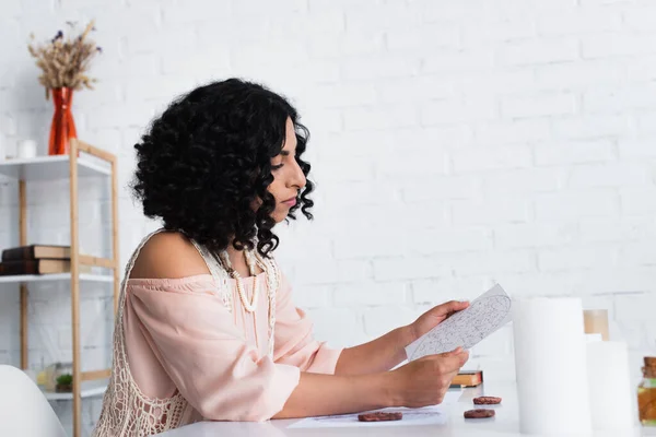 Side view of brunette astrologist holding star chart near clay runes and candles — Photo de stock