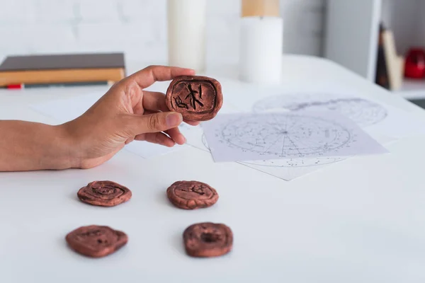 Cropped view of predictor holding clay rune near star charts and blurred candles — Fotografia de Stock