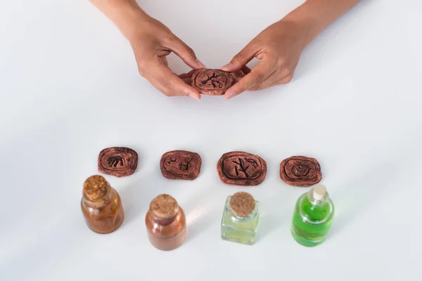 Top view of partial fortune teller holding clay rune near jars with essential oils — Stock Photo