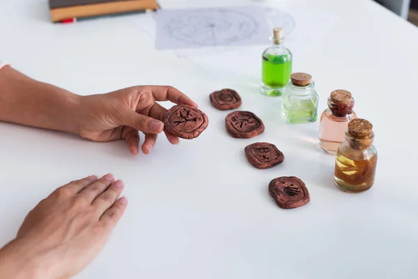 Partial view of fortune teller near clay runes and bottles with essential oils — Stock Photo