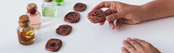 Cropped view of predictor holding clay rune near bottles with essential oils, banner — Photo de stock