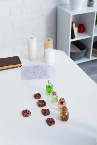 Clay runes and bottles with essential oils near star charts and candles on white table — стоковое фото