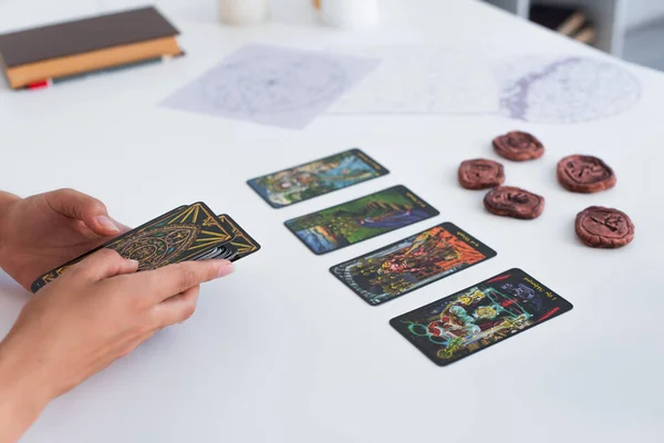 KYIV, UKRAINE - JUNE 29, 2022: cropped view of fortune teller near tarot cards and blurred celestial charts — Photo de stock