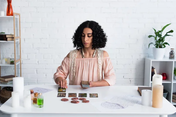 KYIV, UKRAINE - JUNE 29, 2022: brunette fortune teller predicting on tarot cards and clay runes at home — Fotografia de Stock