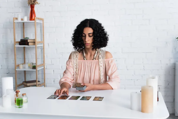 KYIV, UKRAINE - JUNE 29, 2022: young brunette medium near tarot cards and candles at home — стокове фото