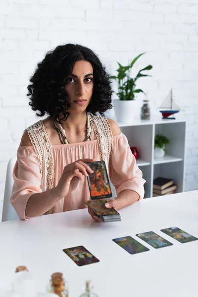 KYIV, UKRAINE - JUNE 29, 2022: young soothsayer showing tarot cards and looking at camera — Photo de stock