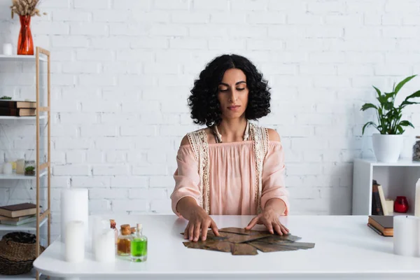 Brunette fortune teller predicting on tarot cards near candles and bottles with essential oils — Stock Photo