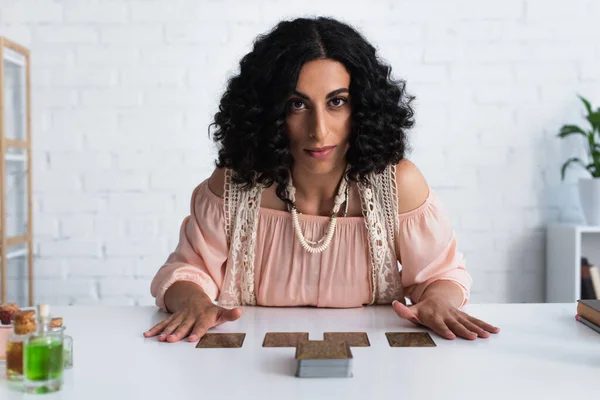 KYIV, UKRAINE - JUNE 29, 2022: young predictor looking at camera while sitting near tarot cards — Stock Photo