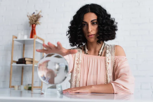 Brunette fortune teller holding hand over crystal ball during spiritual session — Stock Photo