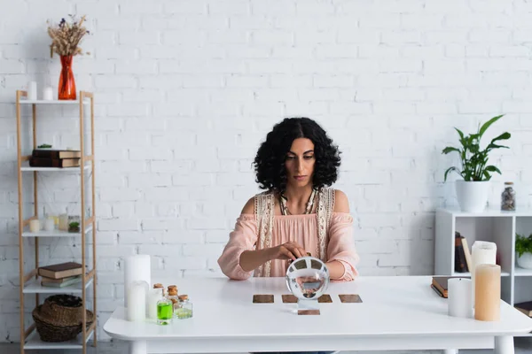 Brunette astrologist near magic sphere and tarot cards during spiritual session at home - foto de stock