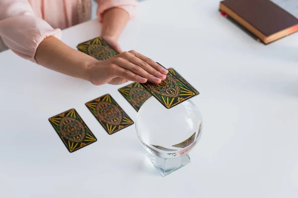 KYIV, UKRAINE - JUNE 29, 2022: high angle view of cropped predictor holding tarot card near magic orb at home — Stock Photo