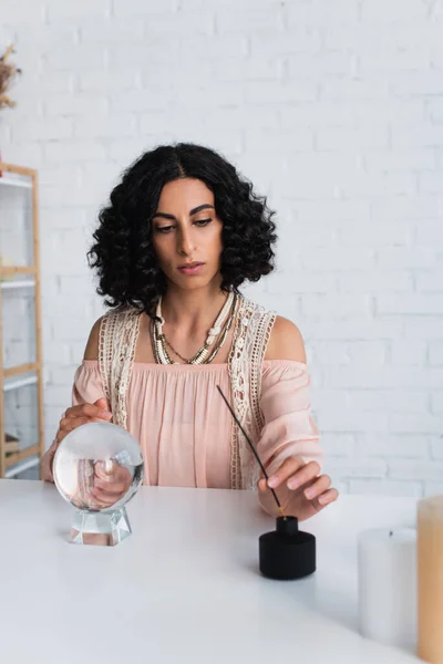 Brunette fortune teller near aroma stick and crystal ball at home — Stock Photo