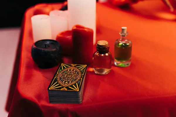 KYIV, UKRAINE - JUNE 29, 2022: tarot cards and bottles with essential oils near candles on red table - foto de stock