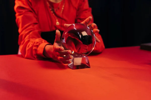 Partial view of fortune teller near crystal ball on red table isolated on black — Foto stock