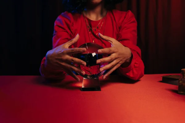 Cropped view of medium holding hands near crystal ball during spiritual session on dark background — Stock Photo