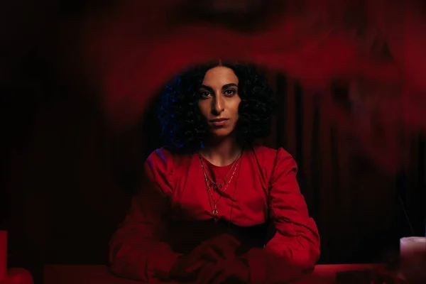 Young fortune teller looking at camera on dark background with red smoke — Stock Photo