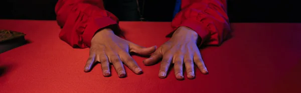 Cropped view of hands of fortune teller on red table isolated on black, banner — Foto stock