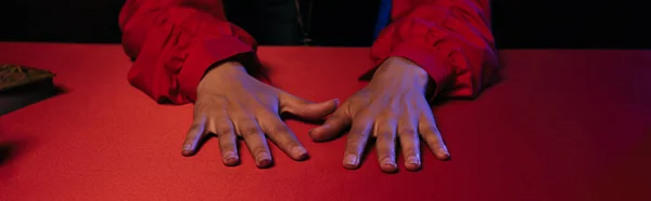 Cropped view of hands of fortune teller on red table isolated on black, banner — Stock Photo