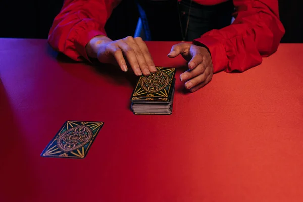 KYIV, UKRAINE - JUNE 29, 2022: cropped view of oracle predicting future on tarot cards on red table isolated on black — Fotografia de Stock