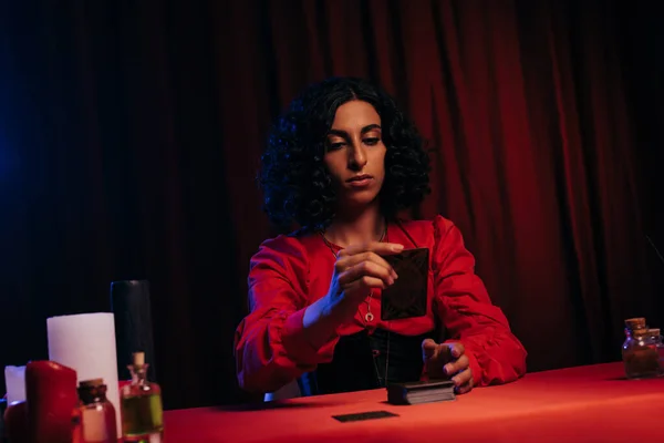 Young fortune teller with tarot cards near candles and essential oils on dark background — Fotografia de Stock