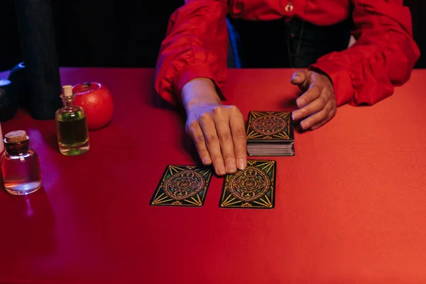 KYIV, UKRAINE - JUNE 29, 2022: partial view of medium predicting future with tarot cards near essential oils on red table — Foto stock